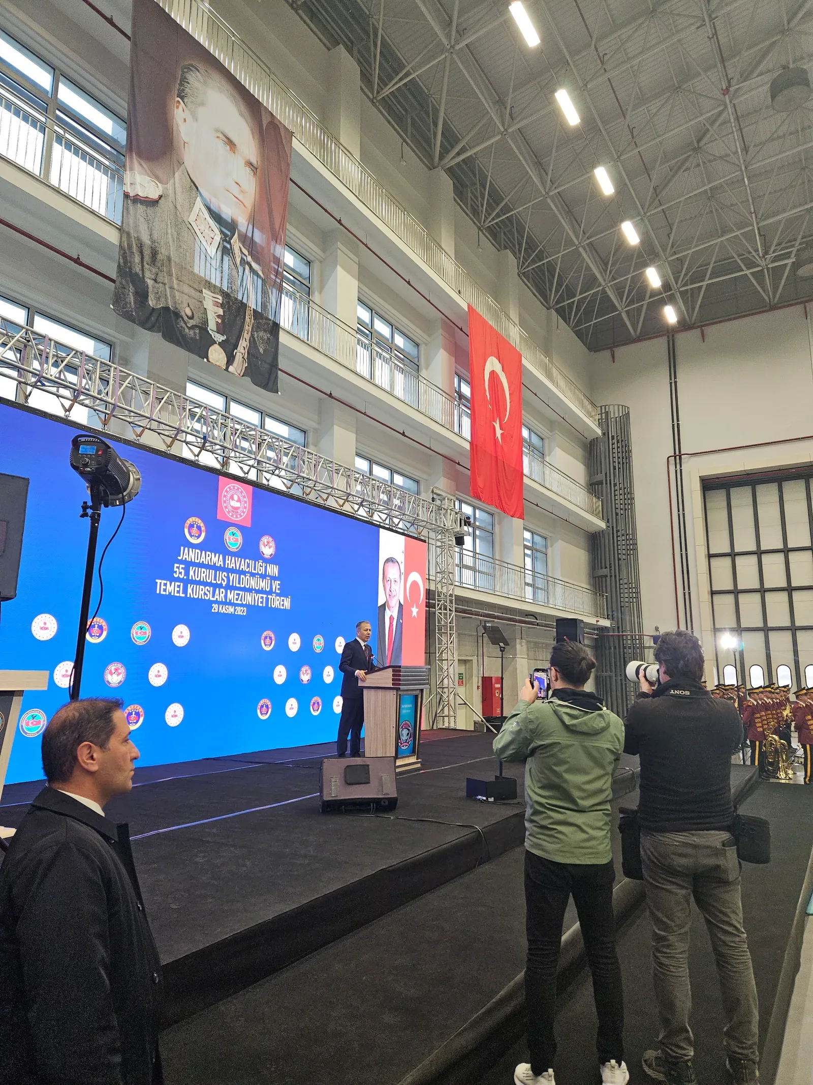 Jandarma Havacılığı mezuniyet töreninde LED ekran önündeki kürsüden yapılan konuşmayı görüntüleyen basın mensupları.