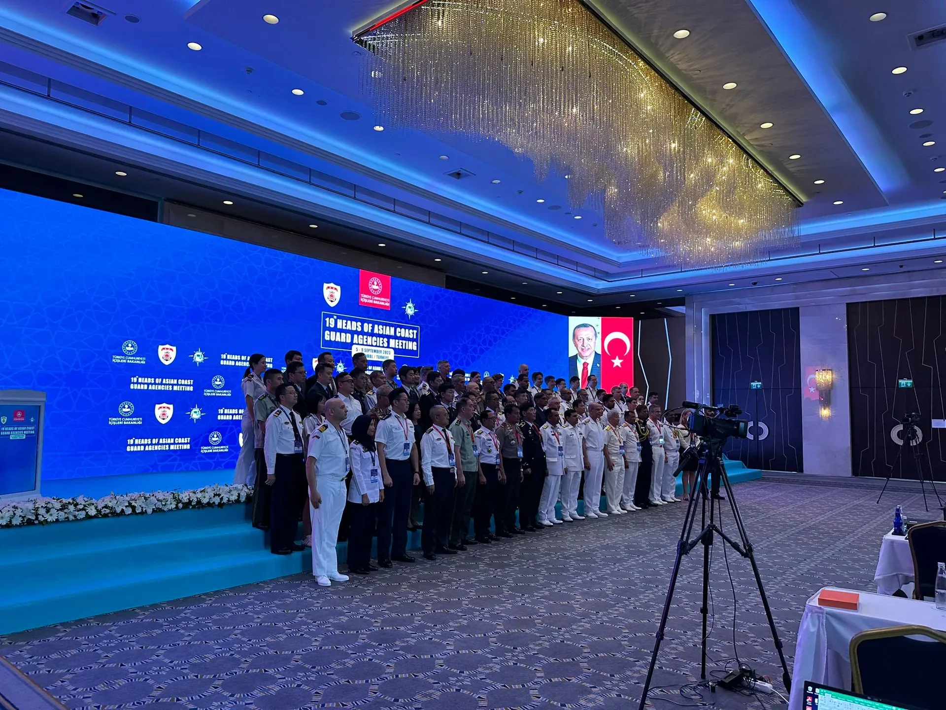 19. Asya Sahil Güvenlik Teşkilatları Liderler Toplantısı katılımcılarının mavi LED sahne önündeki grup fotoğrafı.